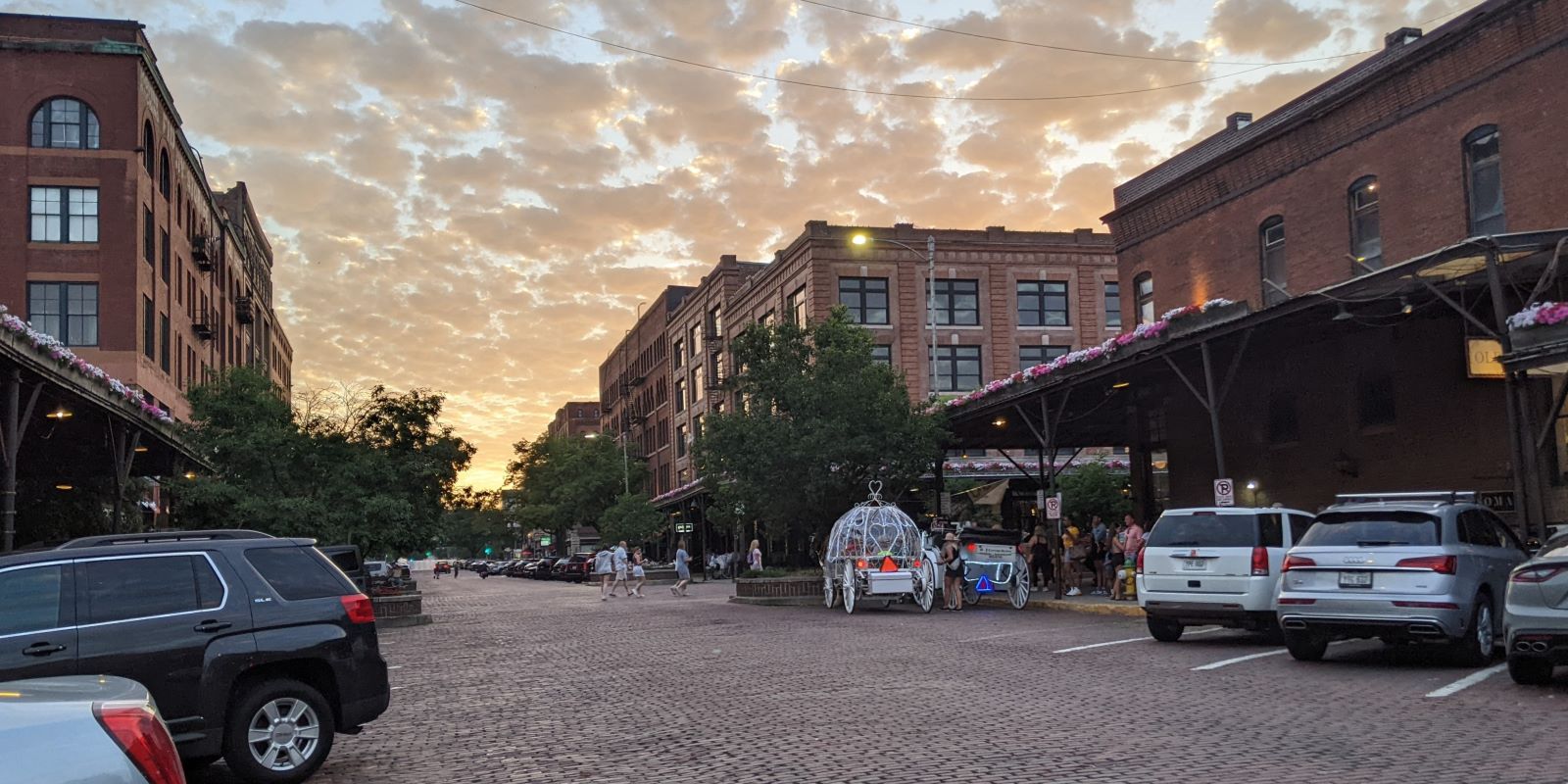 The corner of 11th and Howard Streets in the Old Market at sunset, looking west: brick street, warehouse buildings and flower-lined canopies.