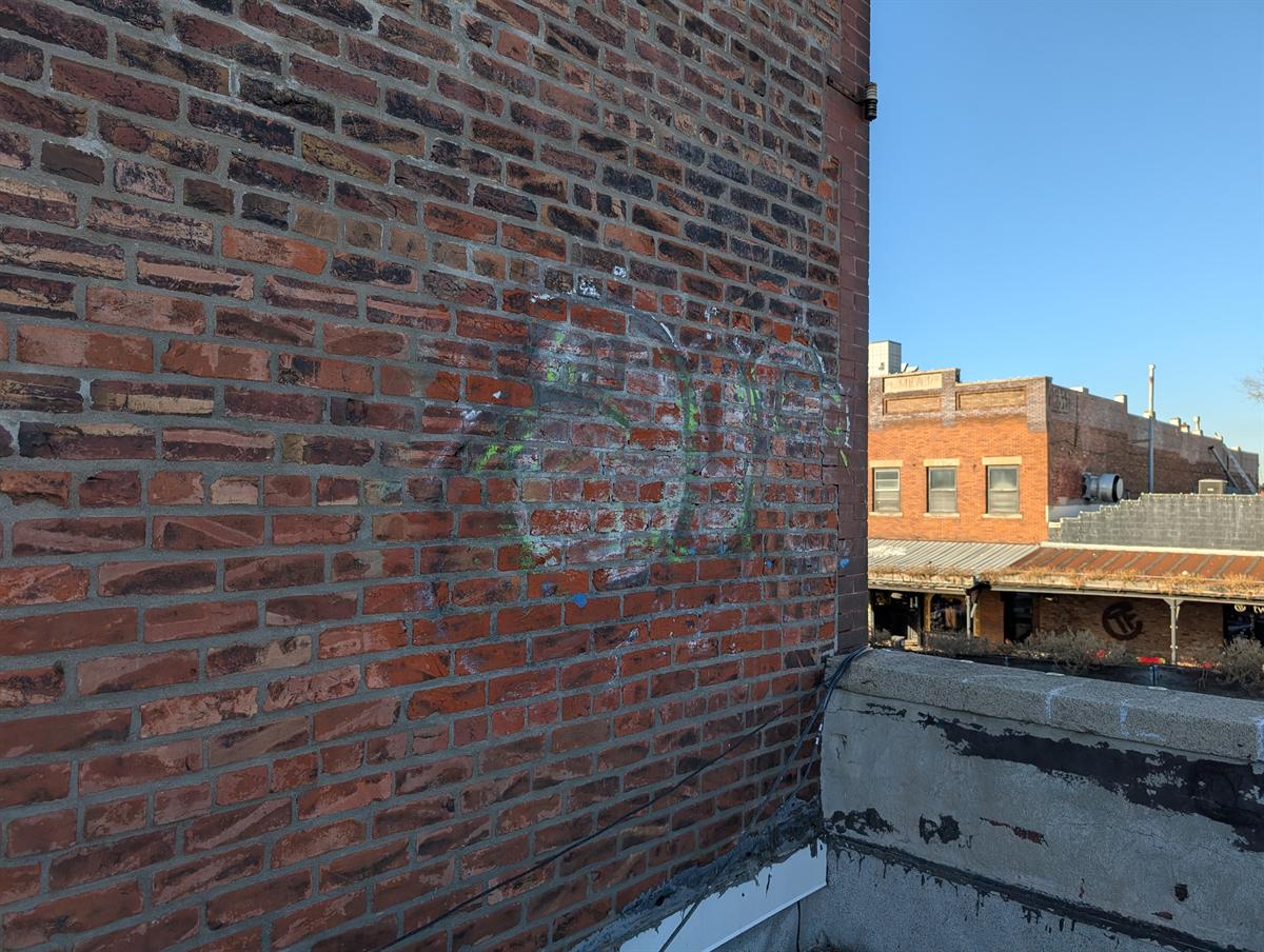After: the same brick wall with the graffiti removed; faint traces remain.